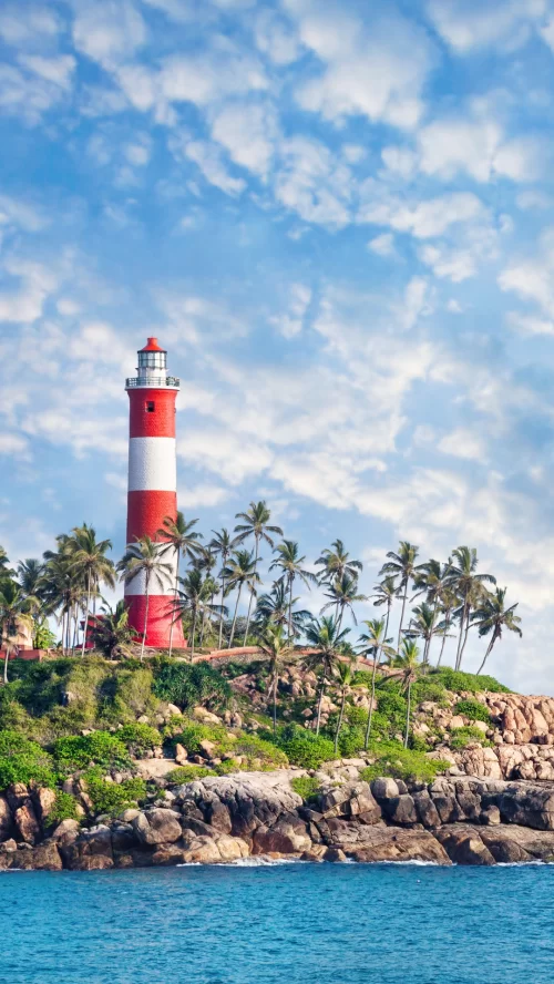 Iconic red and white Vizhinjam Lighthouse surrounded by palm trees at Kovalam, Kerala, overlooking the Arabian Sea, a popular coastal attraction included in Kerala tour packages.