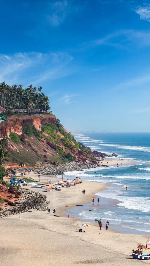 Scenic Varkala Beach with red cliffs, palm-lined shores, and waves of the Arabian Sea in Kerala, a stunning coastal destination featured in Kerala tour packages.