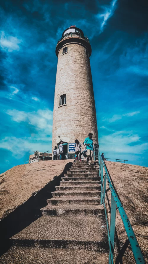 Historic lighthouse at Mahabalipuram, Tamil Nadu, rising above stone steps under a dramatic blue sky, a coastal heritage attraction featured in Tamil Nadu tour packages.
