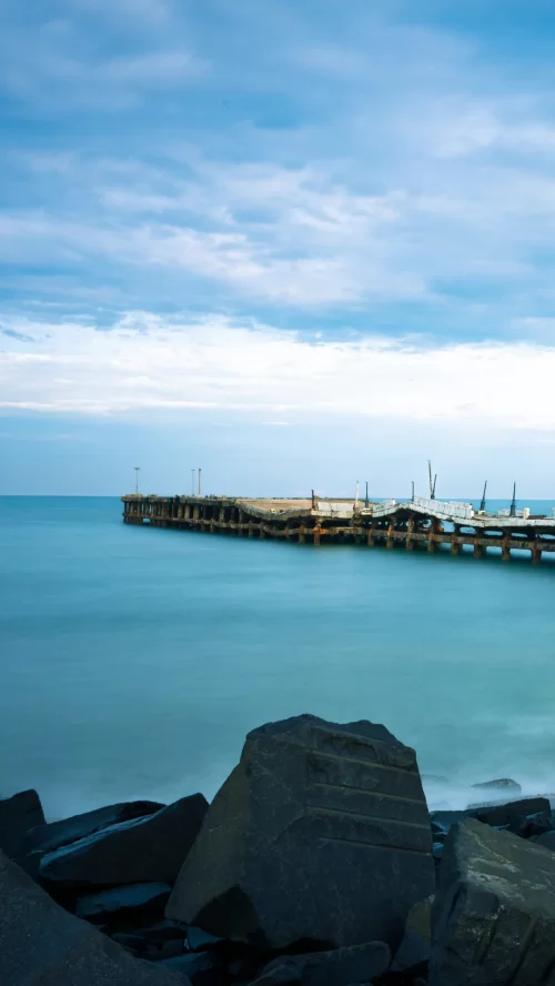 Serene view of Puducherry Pier extending into the calm blue waters of the Bay of Bengal under a cloudy sky, a peaceful coastal attraction featured in Tamil Nadu tour packages.