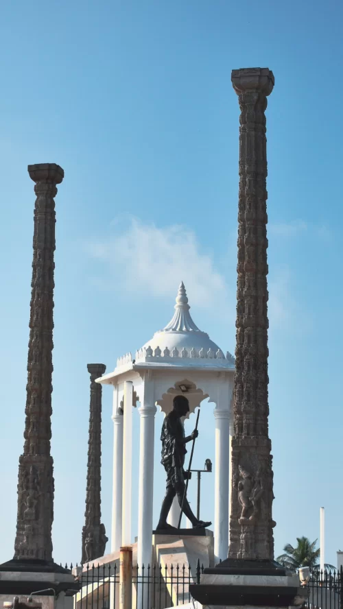 Mahatma Gandhi statue framed by historic stone pillars at the Promenade in Puducherry, Tamil Nadu, under a clear blue sky, a popular landmark featured in Tamil Nadu tour packages.