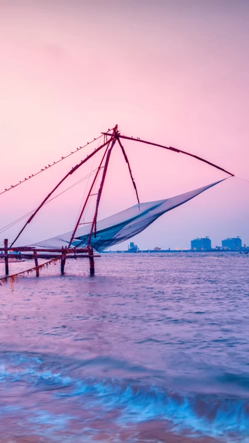 Traditional Chinese fishing nets along the waterfront in Kochi, Kerala, set against a pastel sunset sky and calm backwaters, a historic coastal landmark of Fort Kochi.