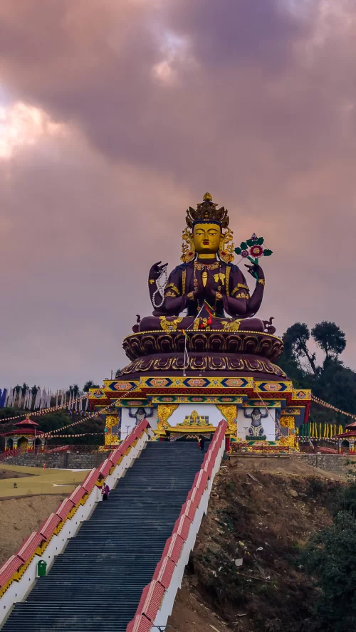 Giant Chenrezig statue overlooking Pelling with grand stRolling green tea estates with misty mountain backdrop in Darjeeling, a scenic hill retreat beautifully featured in West Bengal tour packages.aircase and monastery setting under dramatic sky, a spiri
