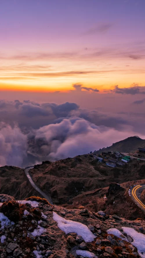 Dramatic sunrise above rolling clouds and winding mountain roads in Zuluk, a breathtaking Himalayan destination featured in Sikkim tour packages.