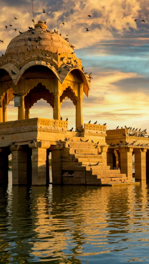 Gadisar Lake Jaisalmer in Rajasthan at sunset, featuring golden chhatri pavilion and birds, perfect romantic experience Rajasthan tour package