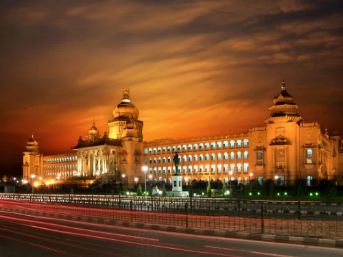 Vidhana Soudha Bangalore nightfall sunset glow, illuminated domes pillars arches lights traffic trails fences, perfect Karnataka tour package.