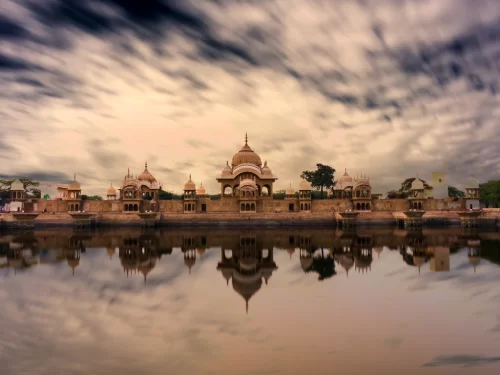 Vishram Ghat temples Mathura reflected in Yamuna River at dusk under cloudy skies, featuring pink sandstone domes and serene water, perfect spiritual Mathura Vrindavan tour package.