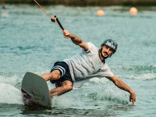 A man wakeboarding across the water, holding onto a tow handle while carving sharply and skimming the surface, creating splashes as he leans low over the board.