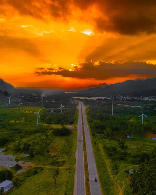 Scenic highway stretching through green landscape with wind turbines under a dramatic sunset sky in Kanniyakumari, a picturesque coastal destination featured in Tamil Nadu tour packages.
