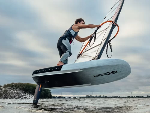A man windsurfing on choppy water, balancing on a hydrofoil board while holding the sail, gliding above the surface under a cloudy sky.