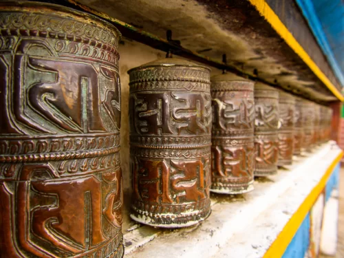 Prayer wheels at Yiga Choeling Monastery in Darjeeling during daytime, featuring rustic metal carvings and vibrant colors, perfect spiritual Darjeeling tour package