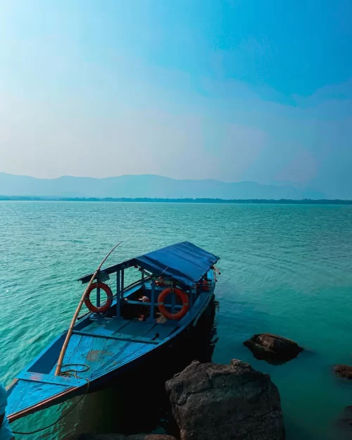 Blue boat anchored at Chilika Lake Odisha with calm green waters and distant hills showcasing scenic views in Odisha tour packages