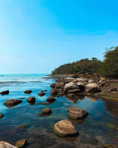 Rocky shoreline at Chilika Lake Odisha with clear turquoise waters and lush greenery showcasing scenic charm in Odisha tour packages