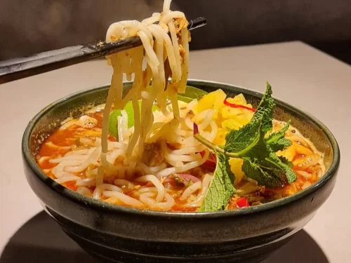 Assamese Laksha in spicy coconut curry broth with rice noodles and lime garnish, authentic Indian Northeastern noodle soup, steaming hot delight.