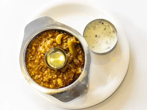 Bisi Bele Bath in spicy lentil rice stew with cashew garnish and yogurt side, authentic Indian Karnataka one-pot meal, steaming hot delight.