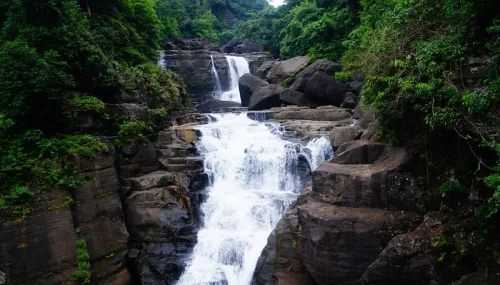 Borhill Falls near Dawki featuring multi-tiered cascading waterfall, dramatic rock formations, and lush green forest canopy, perfect nature experience with Meghalaya tour package.