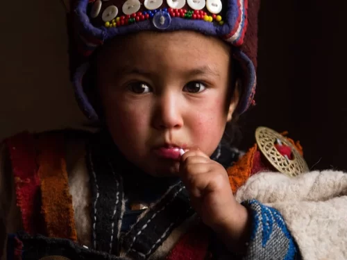 Dha Hanu child during warm light, featuring colorful beaded hat, traditional attire with metal ornaments, perfect cultural experience for Ladakh Dha Hanu tour package. 