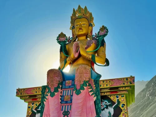 Diskit Gompa Ladakh giant golden Maitreya Buddha statue prayer pose pink base green mountain backdrop Nubra Valley, perfect spiritual Leh Ladakh adventure package.