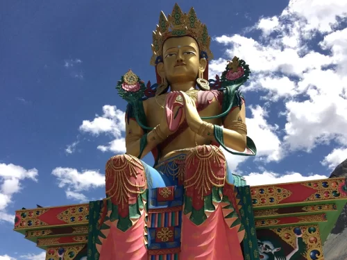 Diskit Gompa Ladakh giant golden Maitreya Buddha statue prayer hands lotus crown pink base green mountain backdrop Nubra Valley, perfect Leh Ladakh spiritual adventure package.