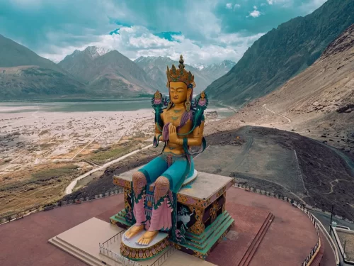 Diskit Gompa Ladakh aerial golden Maitreya Buddha statue snowy peaks Shyok River Nubra Valley desert backdrop, perfect Leh Ladakh spiritual adventure package.
