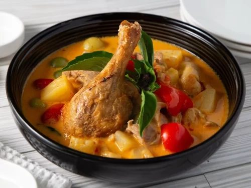 Duck Curry features roasted duck in creamy coconut red curry with pineapple, potato, tomato and basil garnish, authentic Thai-influenced Indian fusion dish.