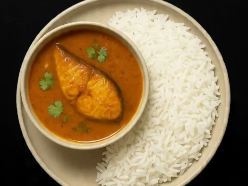 Fish curry features tender fish fillets simmered in aromatic onion-tomato gravy with cilantro garnish, served alongside steamed rice, classic coastal Indian delicacy.