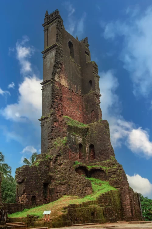 Historic ruins of a red laterite church tower surrounded by greenery in Goa, a fascinating heritage site featured in Goa tour packages.