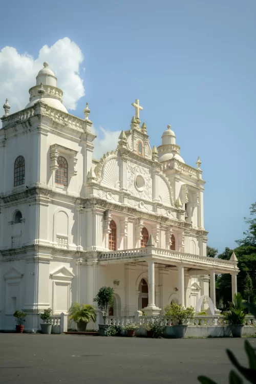 Historic white church with baroque architecture and cross topped facade in Goa, a heritage landmark often featured in Goa tour packages.