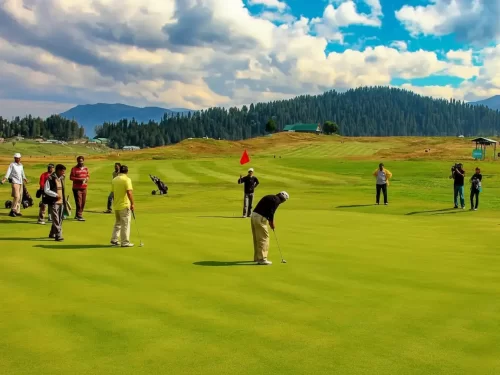 Gulmarg Kashmir golf course green turf players yellow red black clothes flag pine mountains cloudy blue skies, perfect high altitude golf adventure tour package. 