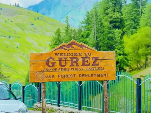 Welcome to Gurez signboard at Gurez Valley during misty weather, featuring pine-covered mountains and green pastures, perfect adventure experience Gurez tour package. 