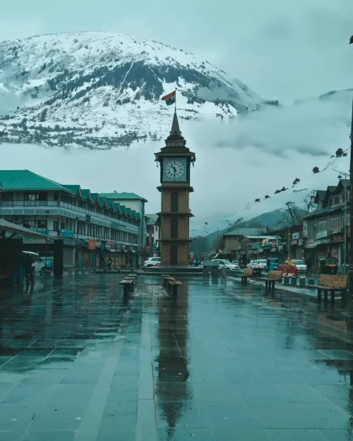 Lal Chowk clock tower in Srinagar Kashmir with snow-covered mountains in the background, a city landmark featured in Kashmir tour packages