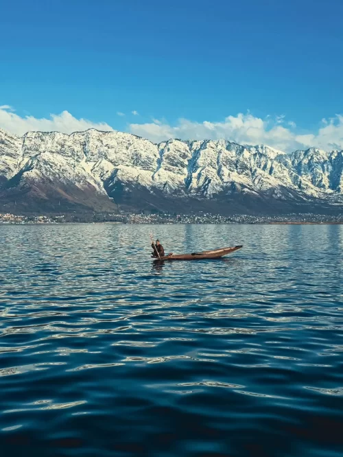 Shikara boat on Dal Lake in Srinagar Kashmir with snow-capped mountains in the background, a timeless experience in Kashmir tour packages