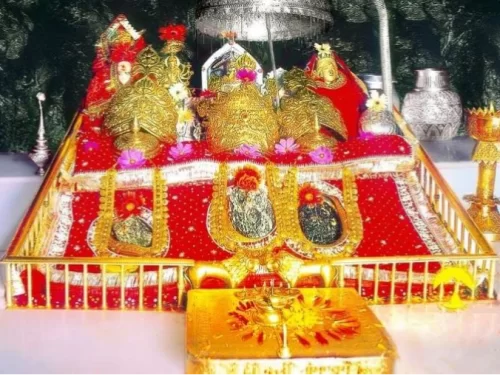 Ornate idols Mata Vaishno Devi shrine Katra Jammu Kashmir closeup, featuring three gold adorned deities red platform flowers lamps offerings, perfect pilgrimage experience Jammu Kashmir tour packages.