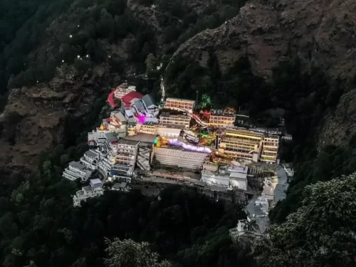 Vaishno Devi Bhawan temple Katra Jammu Kashmir during evening lights, featuring illuminated shrines buildings perched Trikuta mountains forested hills backdrop, perfect pilgrimage experience Jammu Kashmir tour packages.