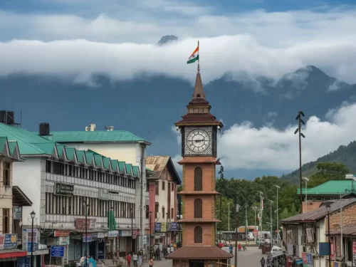 Clock tower Ghanta Ghar at Lal Chowk Srinagar with Indian flag mountain backdrop shops featured in Kashmir Srinagar tour packages