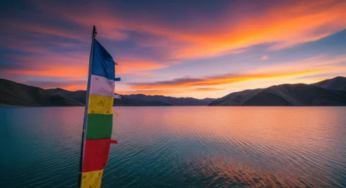 Pangong Lake at Ladakh during sunset, featuring prayer flags and mountain reflections, adventure Leh Ladakh tour package.