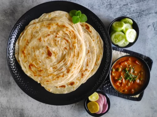Malabar Parotta with flaky layered flatbread served alongside spicy vegetable curry, onions, and lemon, authentic Indian South Indian cuisine delight.