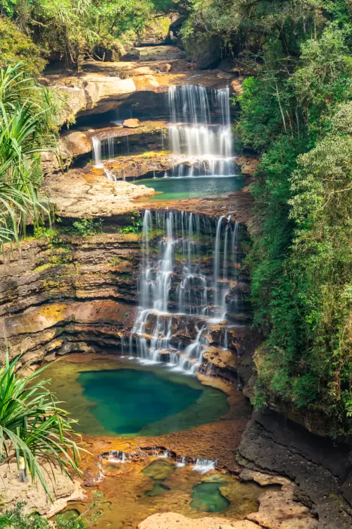 Wei Sawdong Falls in Meghalaya with multi tiered cascading waterfalls and turquoise pools surrounded by lush forest featured in Meghalaya tour packages