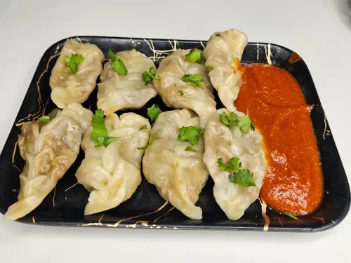 Steamed Momos stuffed with spiced vegetables, garnished with cilantro and served with fiery red chutney, authentic Indian Himalayan street food delight.