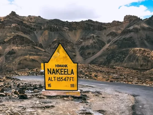 Nakeela pass Himank signboard Ladakh during partly cloudy day, featuring yellow BRO plaque alt 15647 ft, barren rocky mountains winding road, perfect adventure Ladakh tour package.