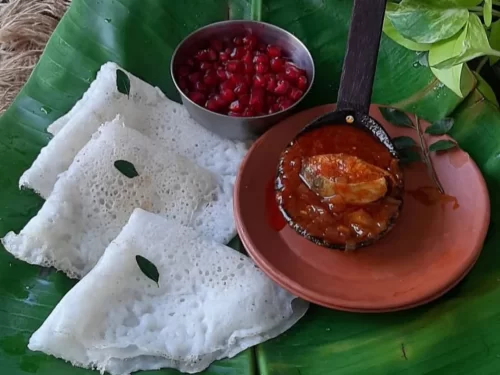 Neer Dosa with soft rice crepes served on banana leaf alongside spicy fish curry and pomegranate, authentic Indian South Indian coastal cuisine delight.