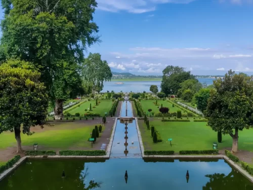 Terraced gardens and fountains at Nishat Garden Srinagar during sunny day, featuring Dal Lake view, chinar trees and pool reflections, perfect romantic experience in Srinagar tour package.