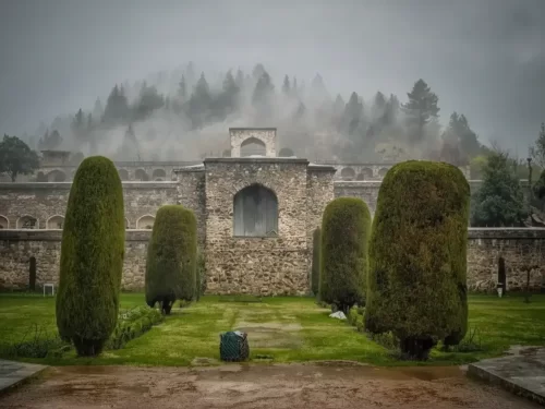 Pari Mahal terraced Mughal garden stone arches manicured lawns conifer trees fog-covered Zabarwan hills backdrop, perfect Jammu Kashmir tour packages.
