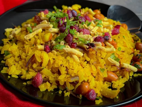 Poha made with flattened rice, peanuts, onions, and curry leaves, garnished with cilantro and pomegranate, authentic Indian breakfast with light flavorful taste.