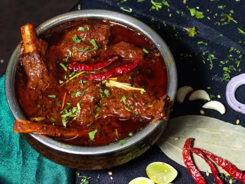 Rogan Josh in aromatic red chili mutton gravy garnished with cilantro and dried chilies, authentic Indian Kashmiri cuisine with rich bold flavors.