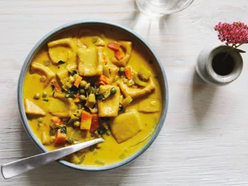 A bowl of skyu, a traditional Ladakhi stew with hand-shaped wheat pasta pieces simmered in a yellow, mildly spiced broth with mixed vegetables.
