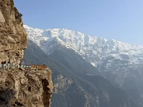 Suicide Point Kalpa Kinnaur winter dramatic vista, featuring cliff-edge viewpoint wooden barrier snowy Himalayan peaks blue skies people viewing, perfect Himachal Pradesh tour packages.