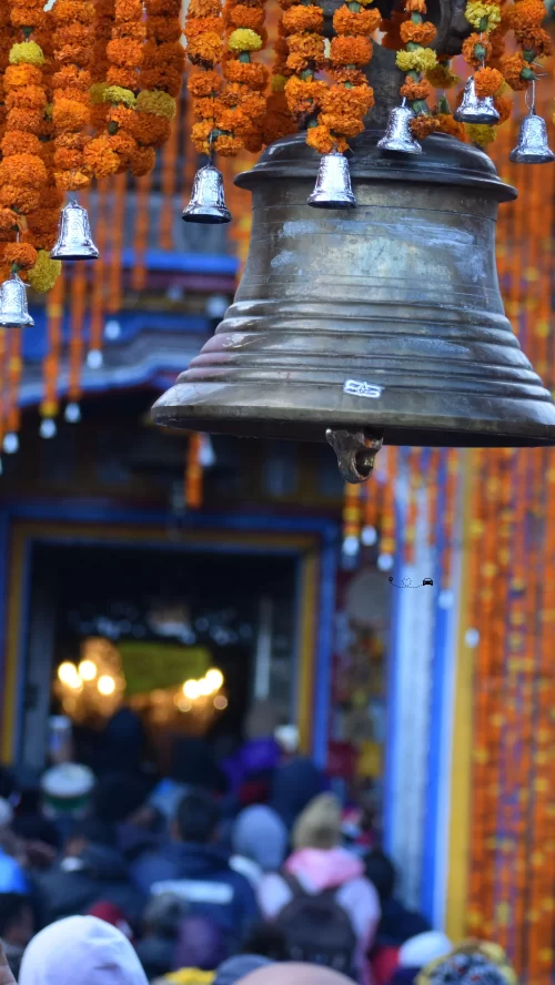 Sacred temple bell adorned with marigold garlands at Kedarnath Temple in Uttarakhand, with devotees gathered at the shrine entrance, a spiritual highlight of Uttarakhand tour packages.