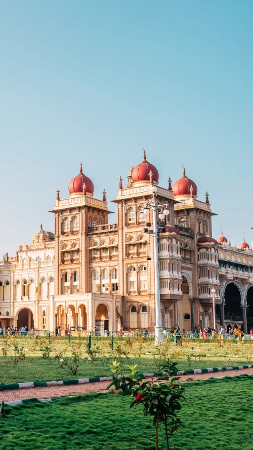 Elegant facade of Mysore Palace with red domes and ornate arches in Mysuru, Karnataka, surrounded by manicured gardens, a royal heritage attraction featured in Karnataka tour packages.