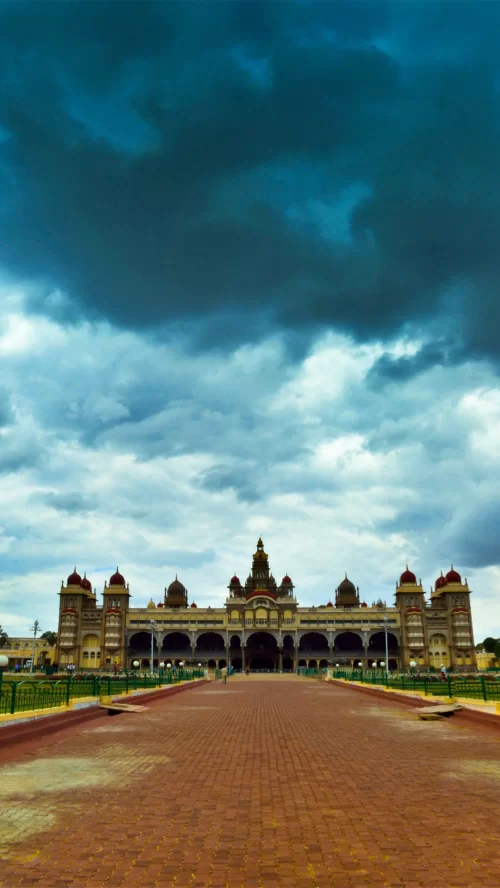 Grand Mysore Palace under dramatic cloudy skies in Mysuru, Karnataka, showcasing Indo-Saracenic architecture and expansive courtyard, a royal heritage attraction featured in Karnataka tour packages.
